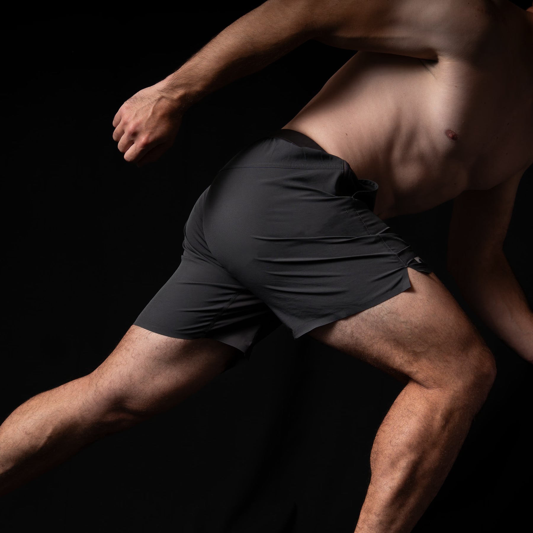 Man in black athletic shorts running against a dark background